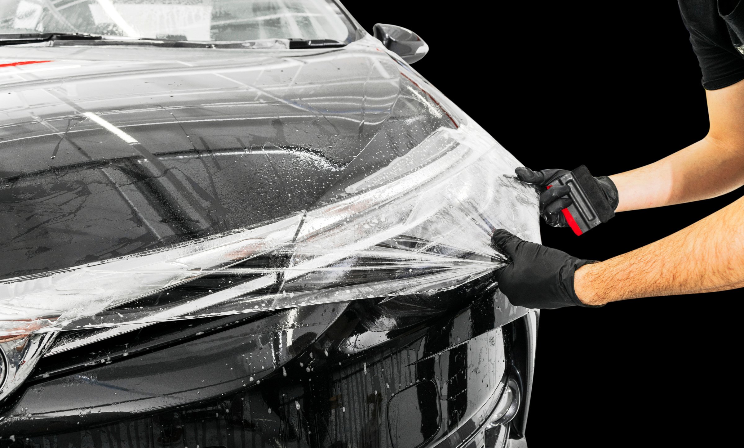 Car wrapping specialist putting vinyl foil or film on car. Protective film on the car. Applying a protective film to the car with tools. Car detailing. Transparent film. Car paint protection. Trimming